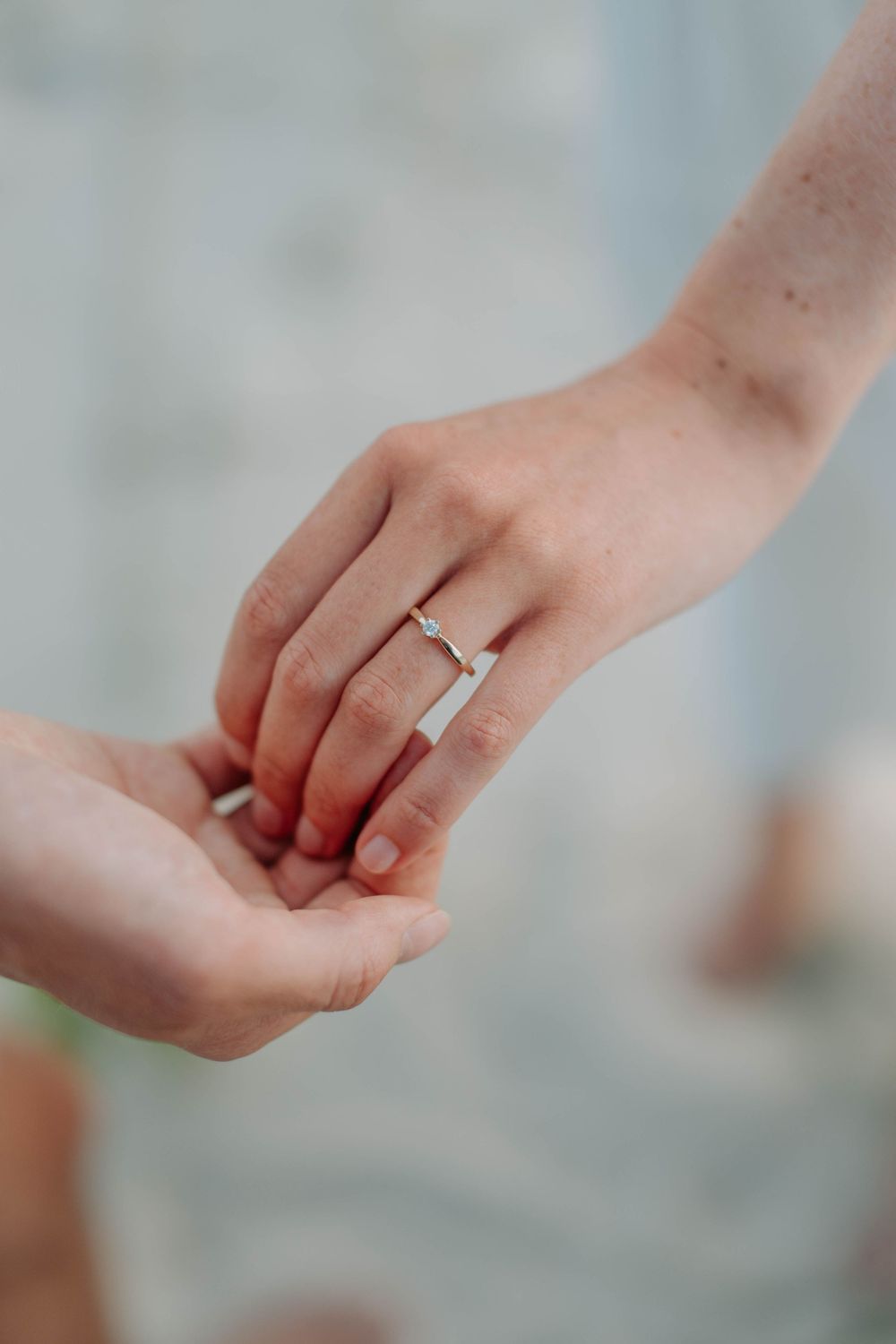 Close-up of two hands holding, woman wearing a delicate diamond engagement ring on her finger.