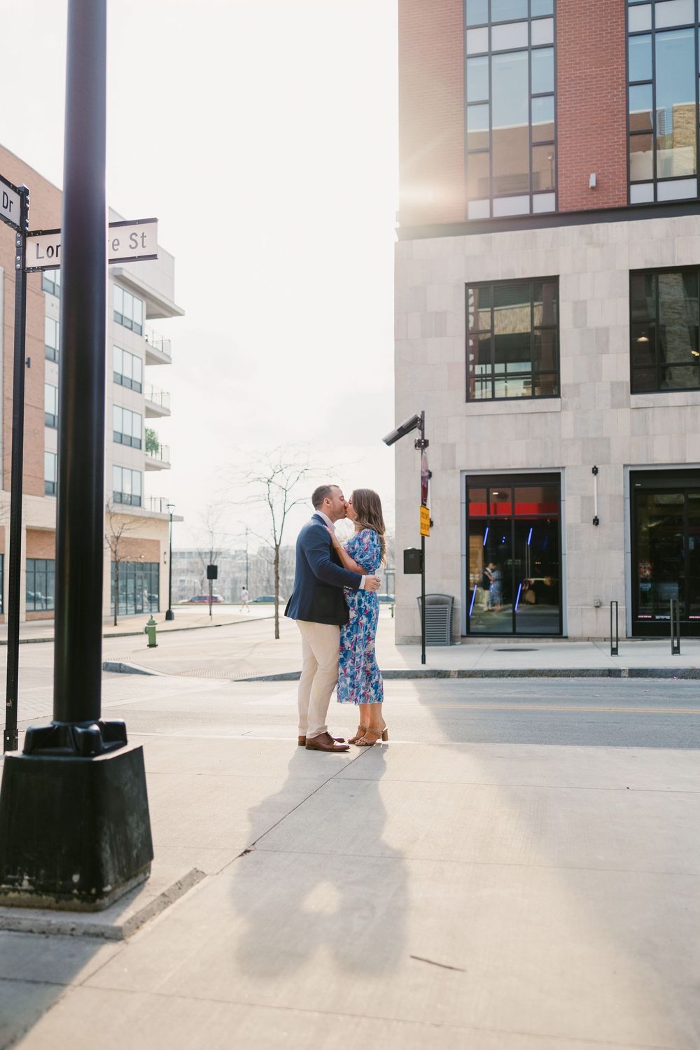 Couple sharing a romantic kiss on a sunny urban street corner Engagement session Bridge Park Dublin Ohio.