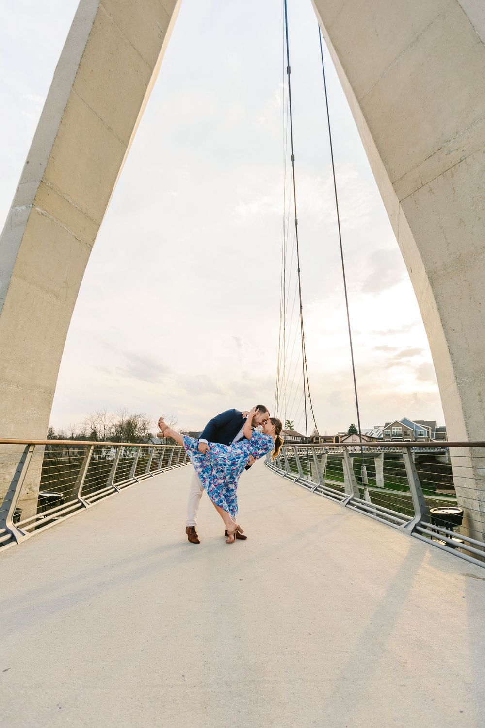 Couple sharing a romantic dip kiss on a modern suspension bridge at sunset.