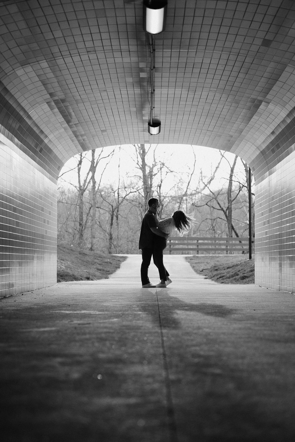 Black and white photo of couple spinning in an arched pedestrian tunnel.