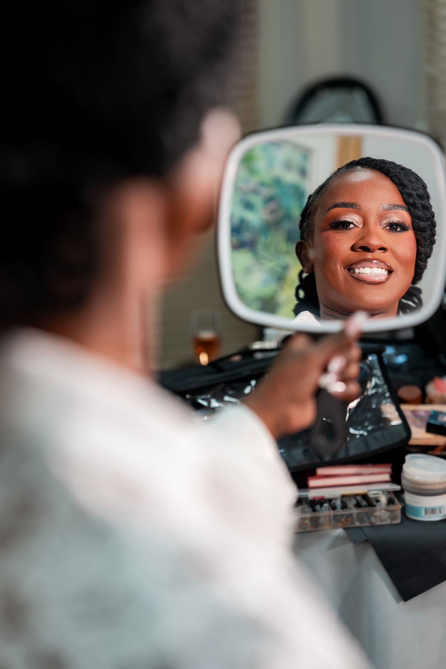 A smiling Black woman checks her makeup in a handheld mirror at a vanity table filled with beauty products. Deerfield Golf Club Newark De