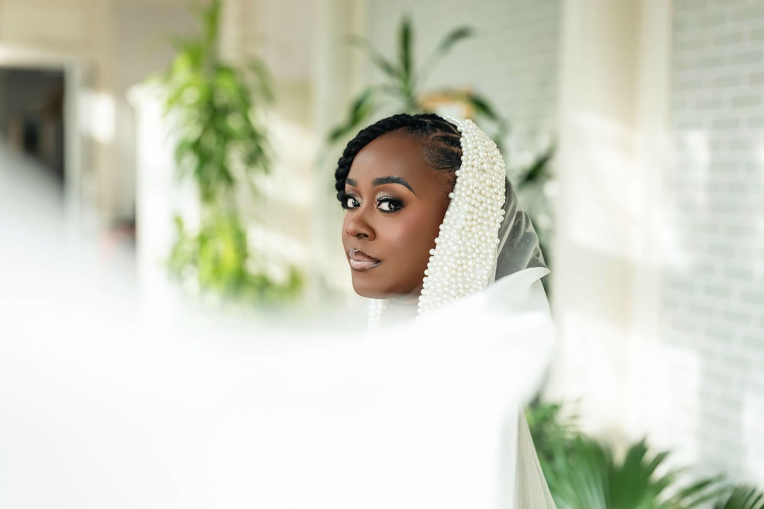 A beautiful Black bride wearing a pearl-adorned white veil & elegant makeup poses gracefully with greenery. Deerfield Golf Club Newark De