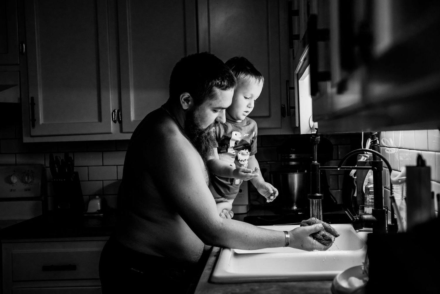 A black and white photo of two people sitting at a kitchen counter in dim lighting looking at something together.
