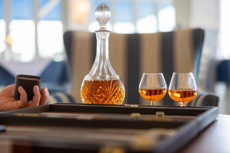 Elegant crystal decanter with amber whiskey beside two snifter glasses on a wooden serving tray.