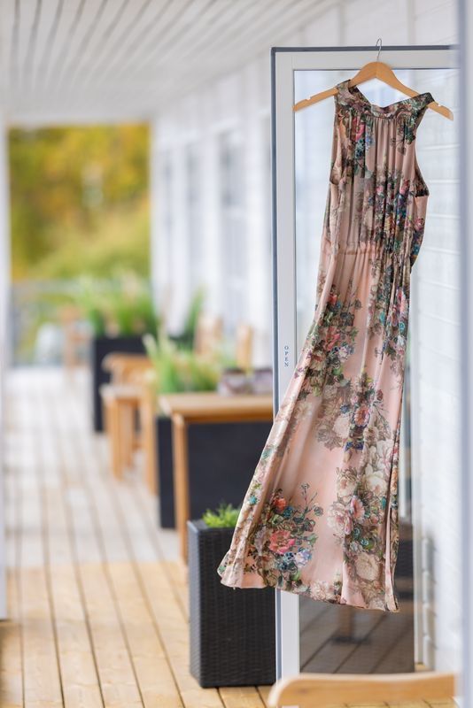 Floral maxi dress on wooden hanger displayed outdoors on a porch with blurred garden background.