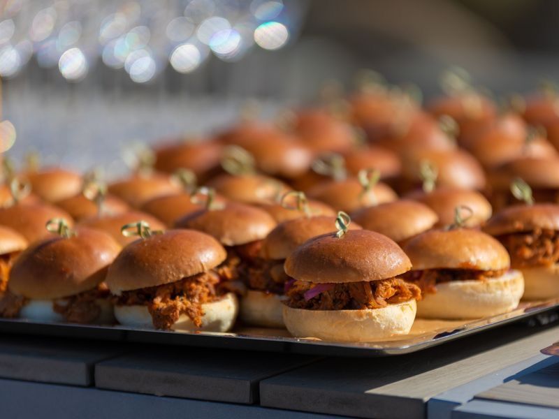 Tray of mini pulled pork sliders on brioche buns served at a catering event.