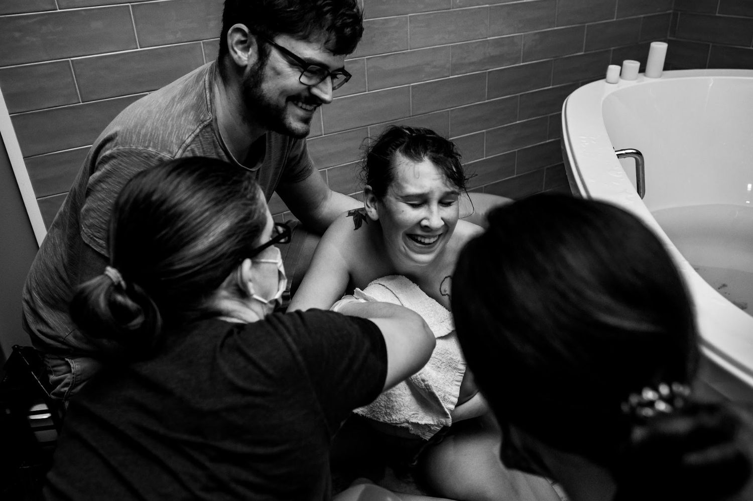 Black and white image showing emotional birthing scene in bathtub with medical team providing support.