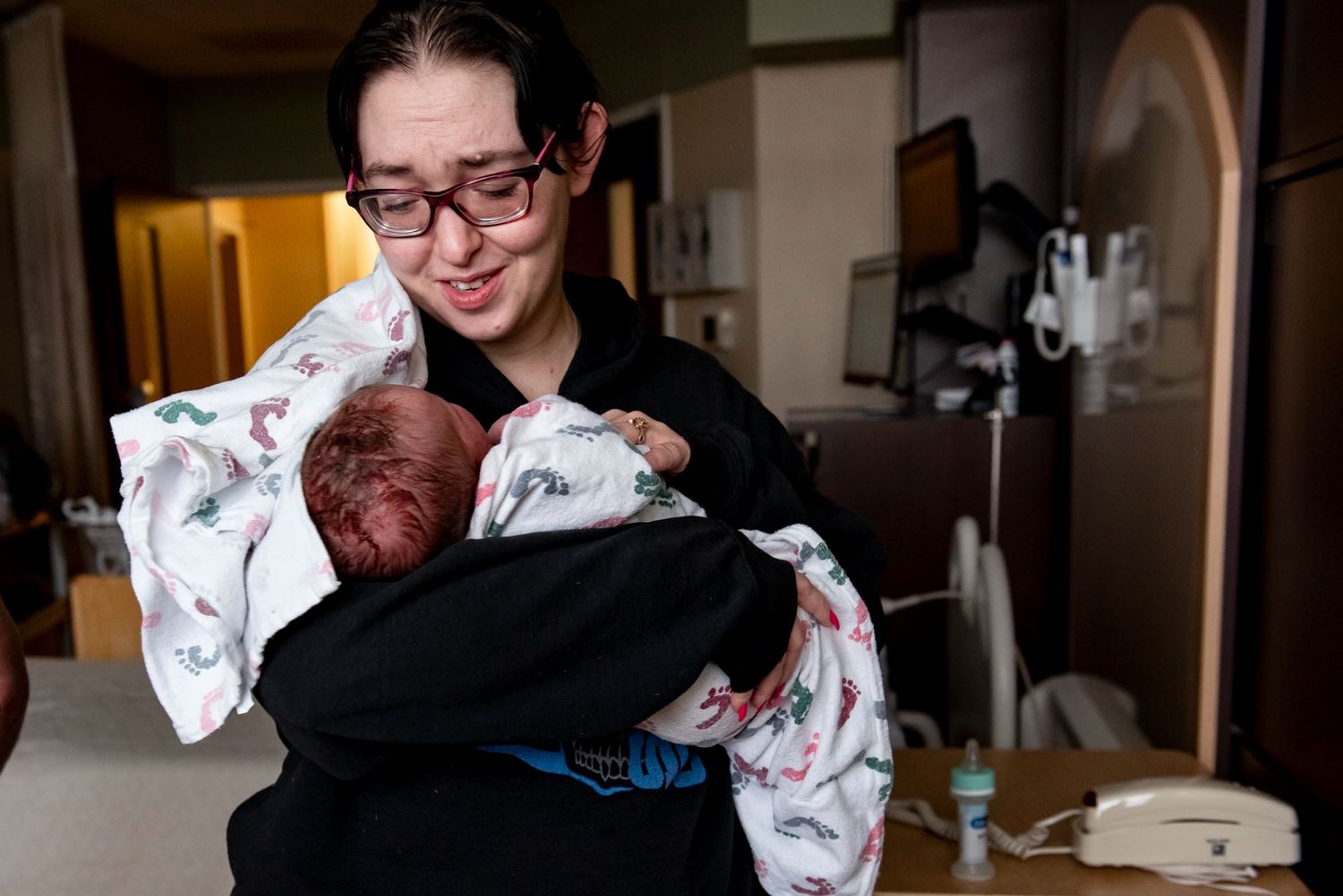 A auntie in black holds a swaddled newborn wrapped in patterned fabric.