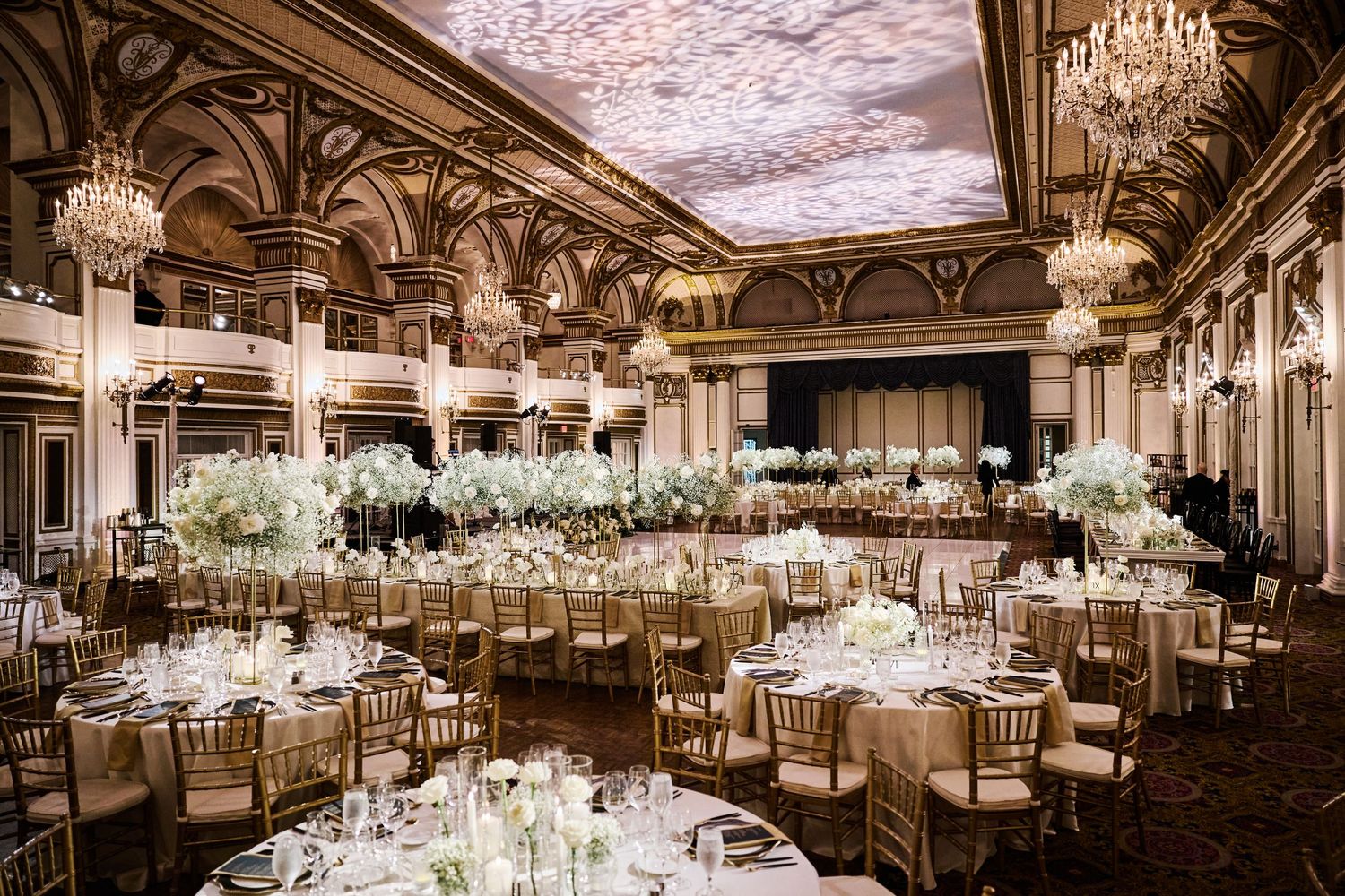 An elegant ballroom set for a wedding reception with crystal chandeliers and ornate architectural details.