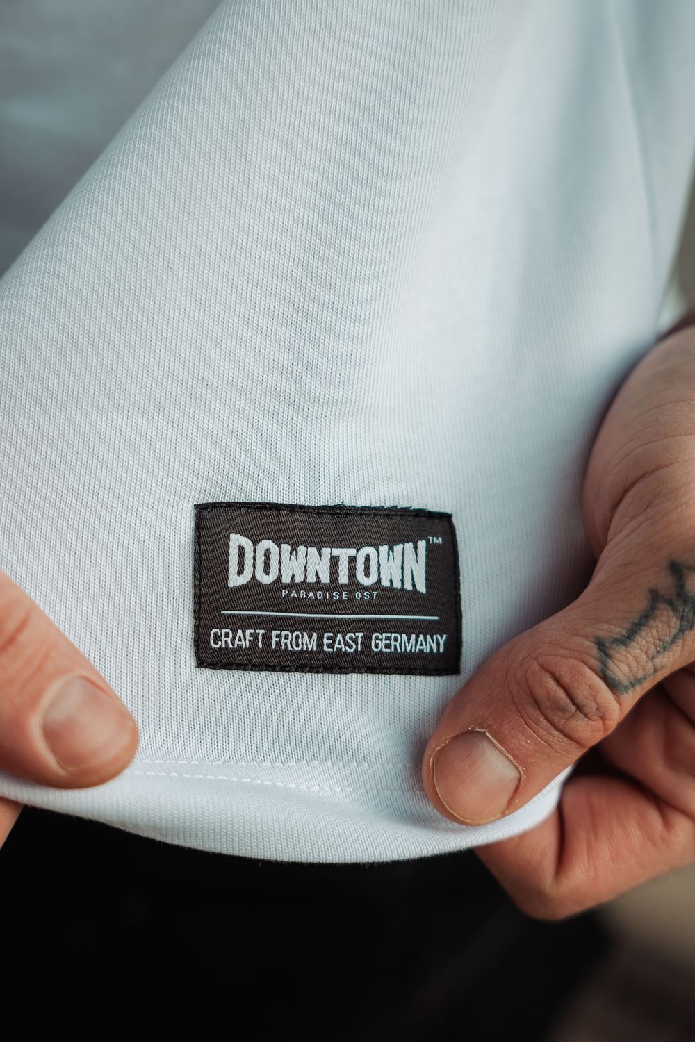Close-up of a Downtown Paradise DDT black label on a white shirt reading Craft From East Germany.