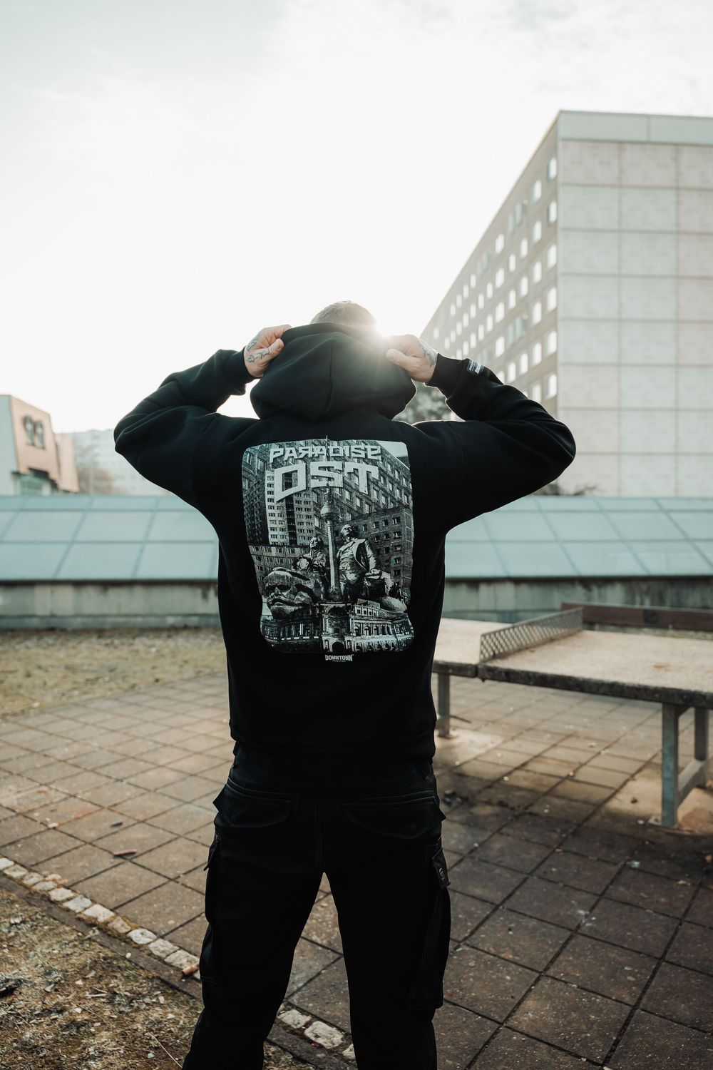 Person wearing a black Downtown Paradise DDT hoodie outdoors with urban buildings in the background.