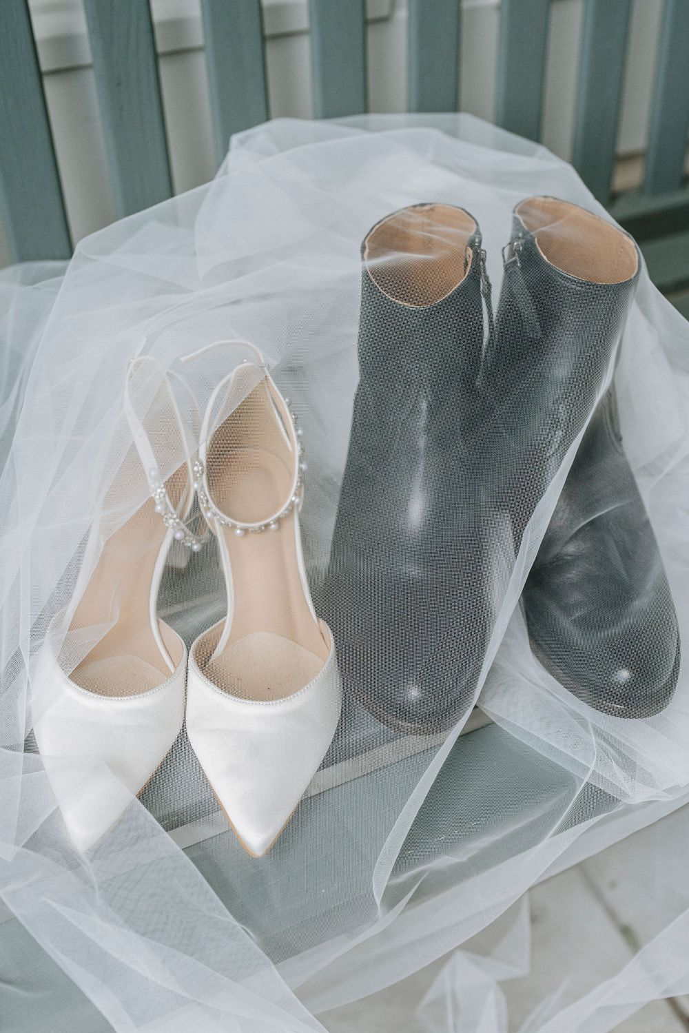 White bridal heels with pearl ankle straps beside clear rain boots on a flowing tulle veil.