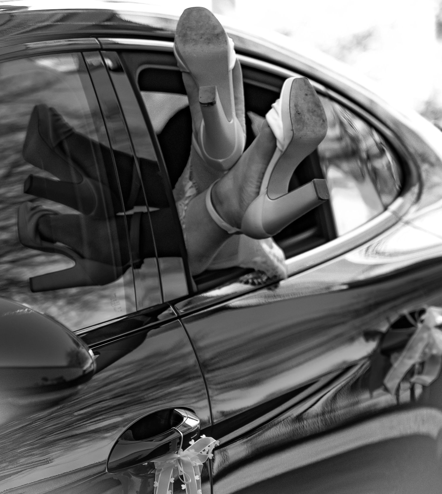 Playful black and white wedding photo of bride with legs sticking out of a luxury car window.