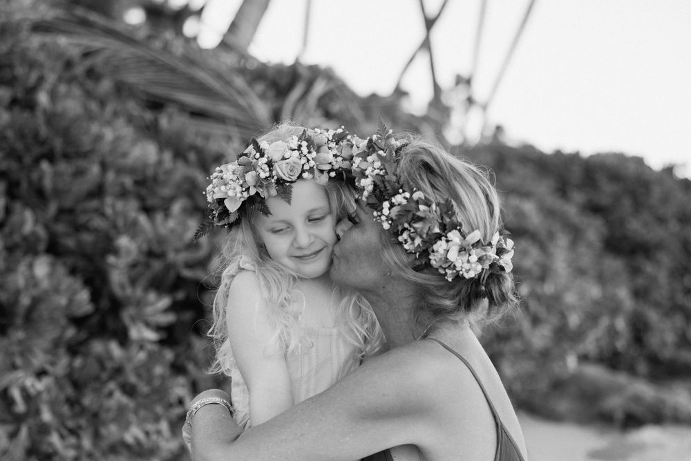 Black and white photo of two girls wearing flower crowns sharing a tender hug outdoors.