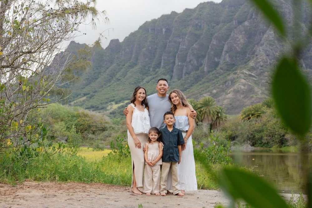 Family of five posing together in front of lush green mountains and tropical landscape in Hawaii.
