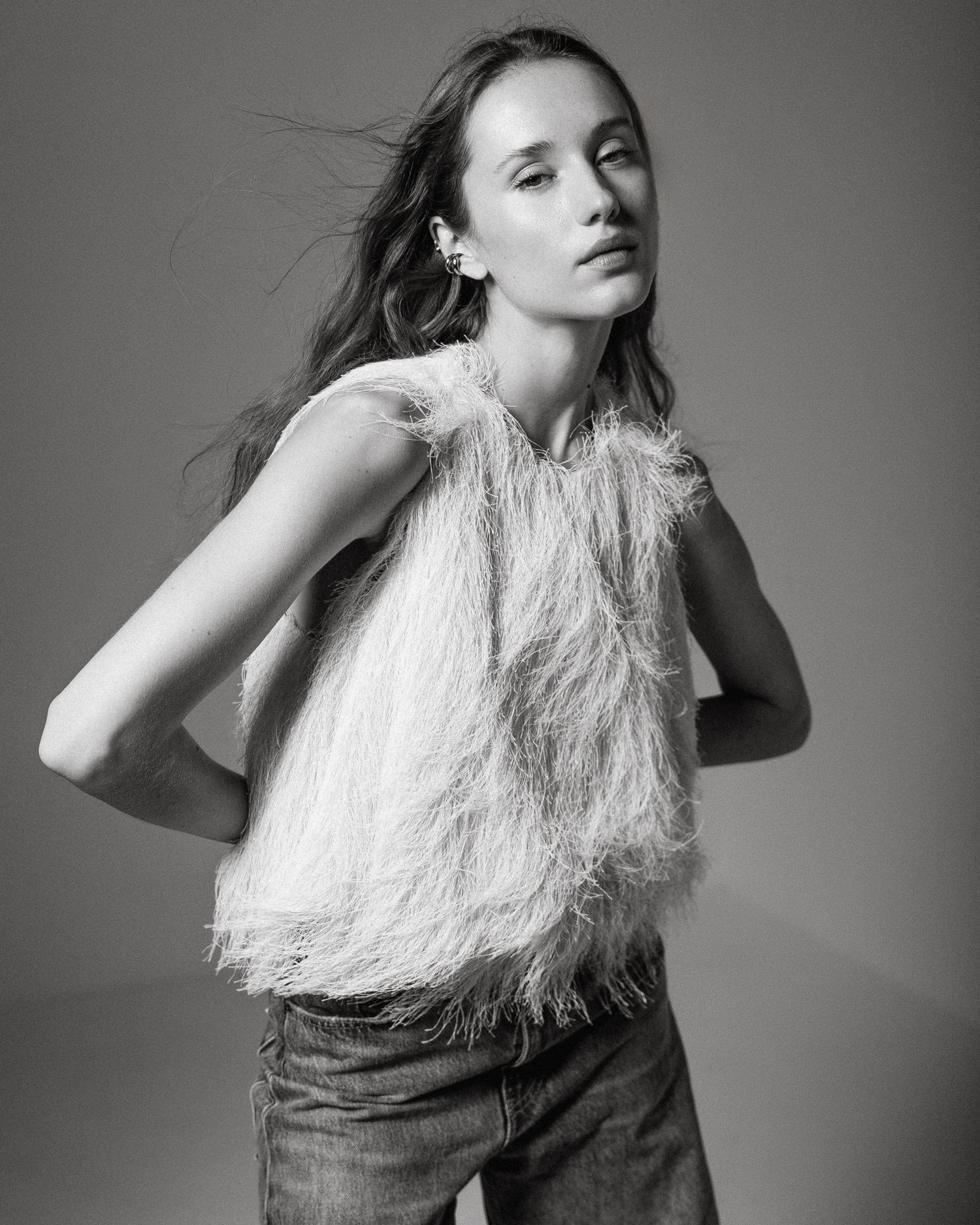 Black and white photo of a young woman wearing a feathered top and jeans, posing elegantly in a studio setting.