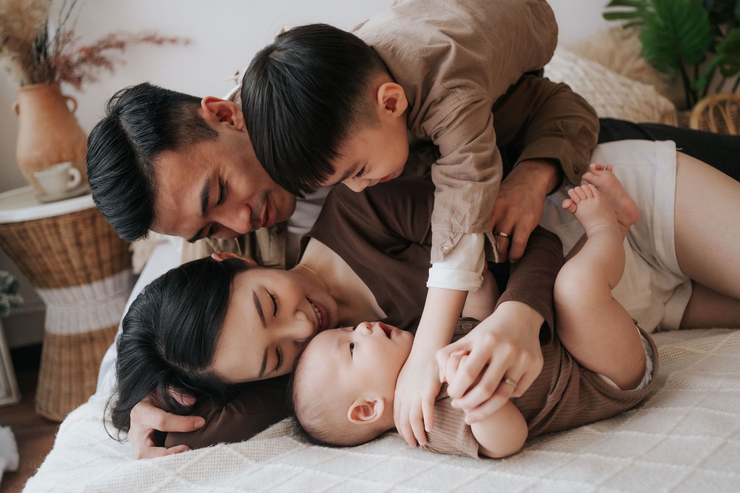 A series of intimate photos showing a family lying together on a white bed in a cozy setting.一組溫馨的照片，展現了一家人在舒適的環境中躺在白色床上。