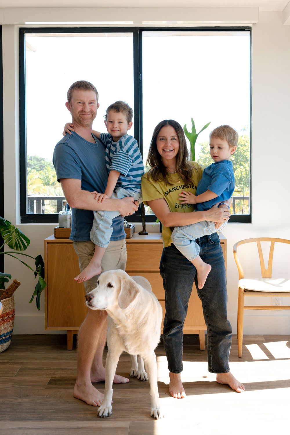 Happy family of four with golden retriever dog posing in modern sunlit home interior.