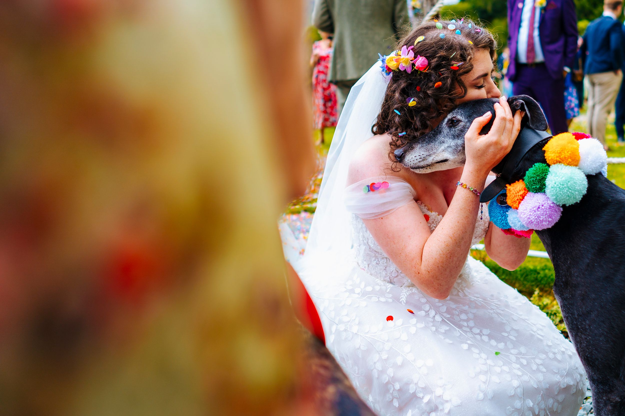 A bride in a white dress hugs a guest warmly during an outdoor wedding celebration with colorful decor.