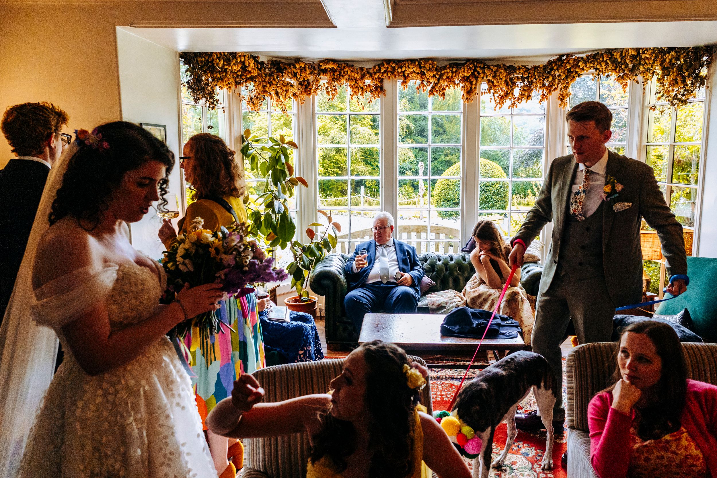 A bride and groom mingle with guests in a warmly decorated living room during their wedding reception at the Lancrigg in Grasmere
