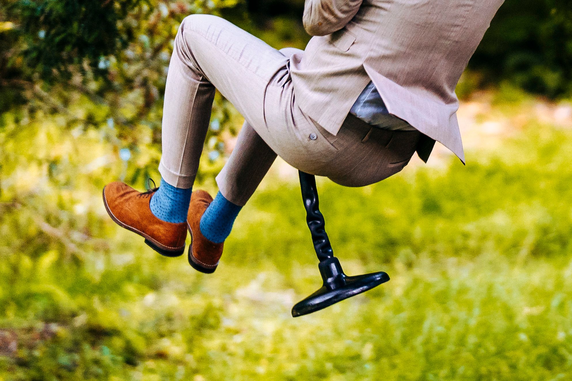A person in beige trousers and bright blue socks swings through the air holding a black cane in a grassy outdoor setting.