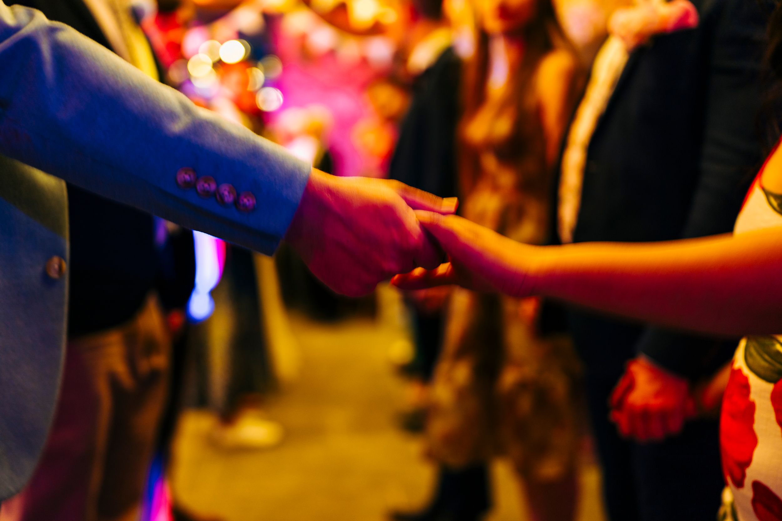 Close-up of a couple holding hands on a colorful illuminated dance floor during a lively wedding reception.