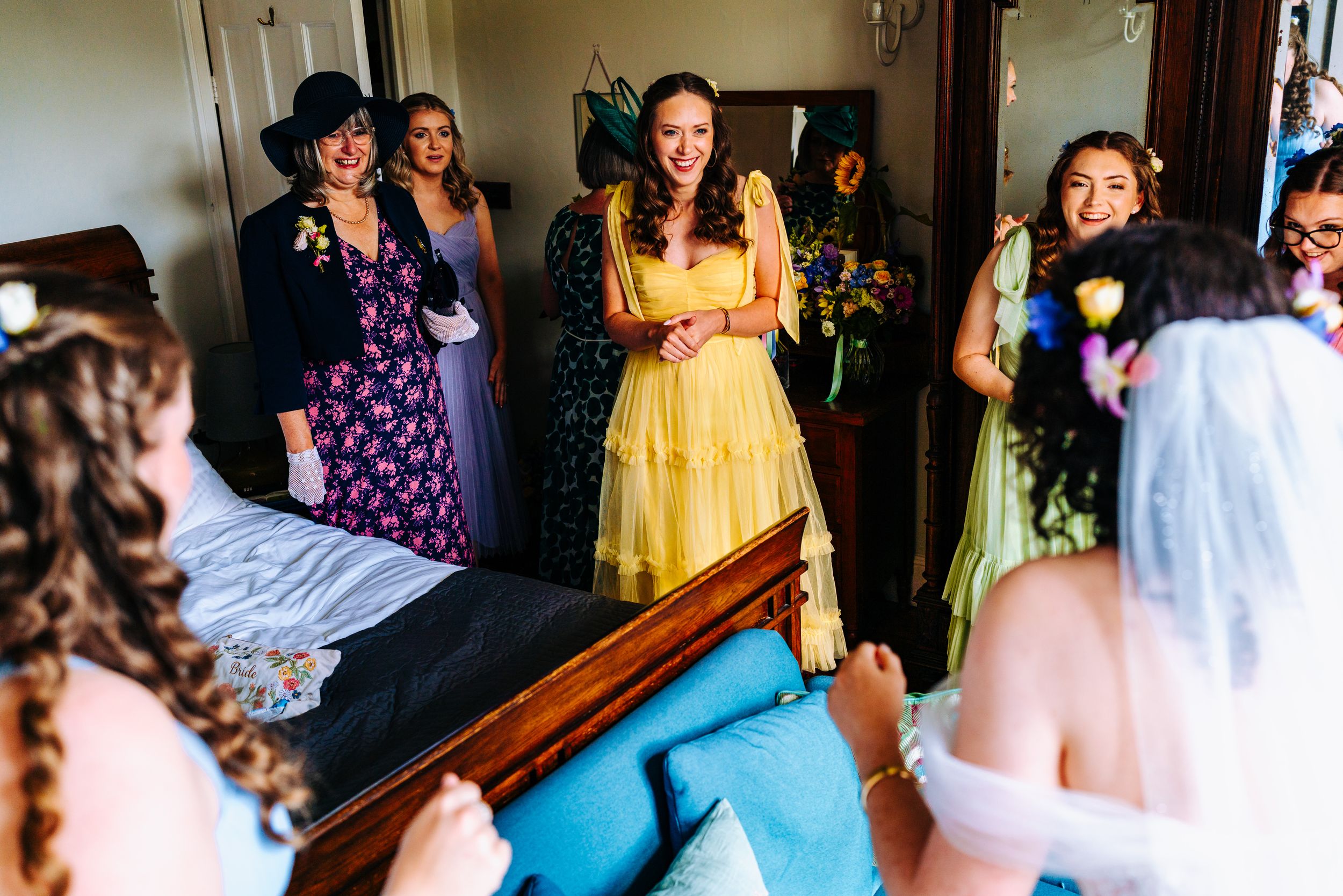 Bridesmaids in colorful dresses react with joy seeing bride in stunning white wedding gown.