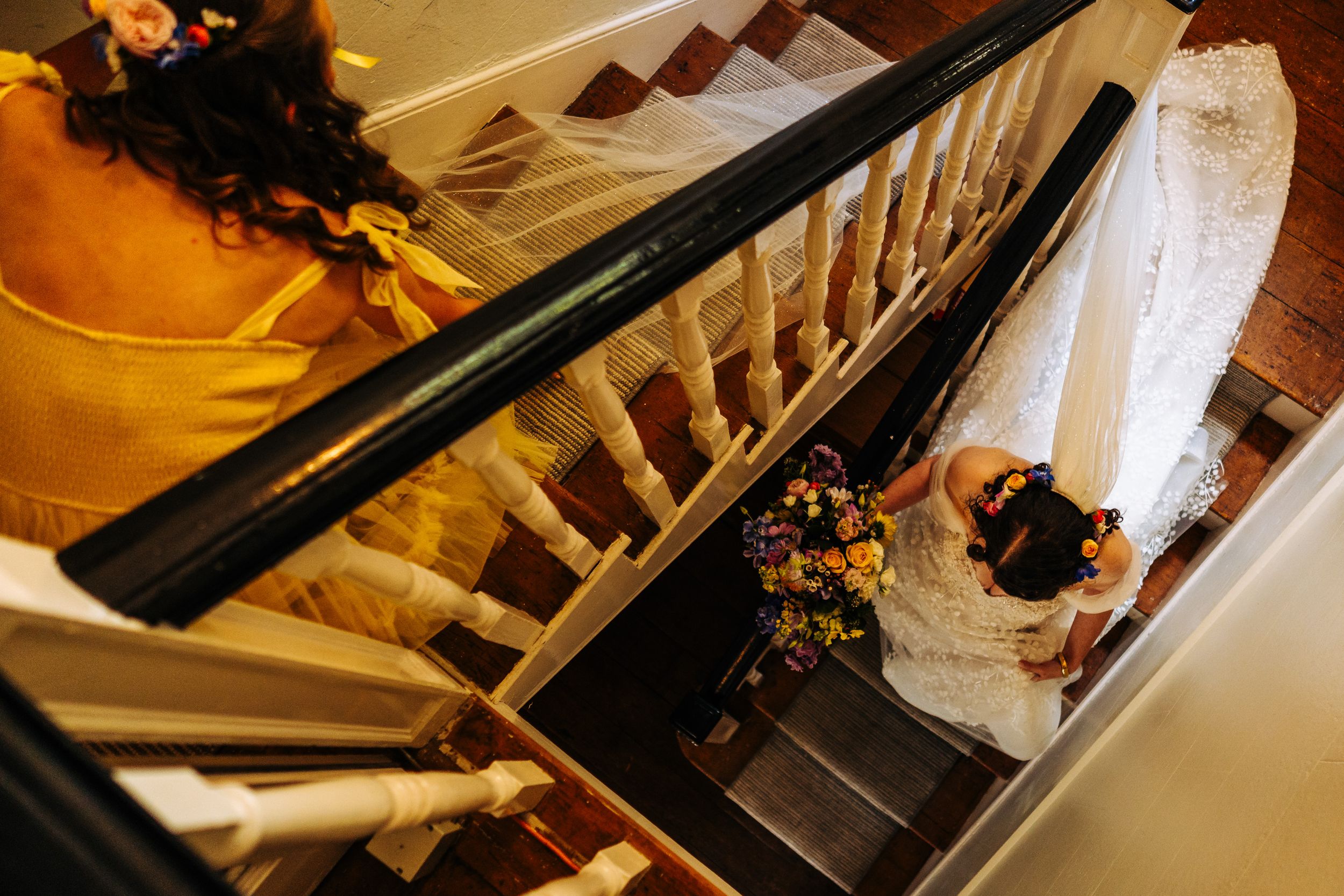Aerial view of bride descending grand staircase in lace wedding dress holding bouquet.