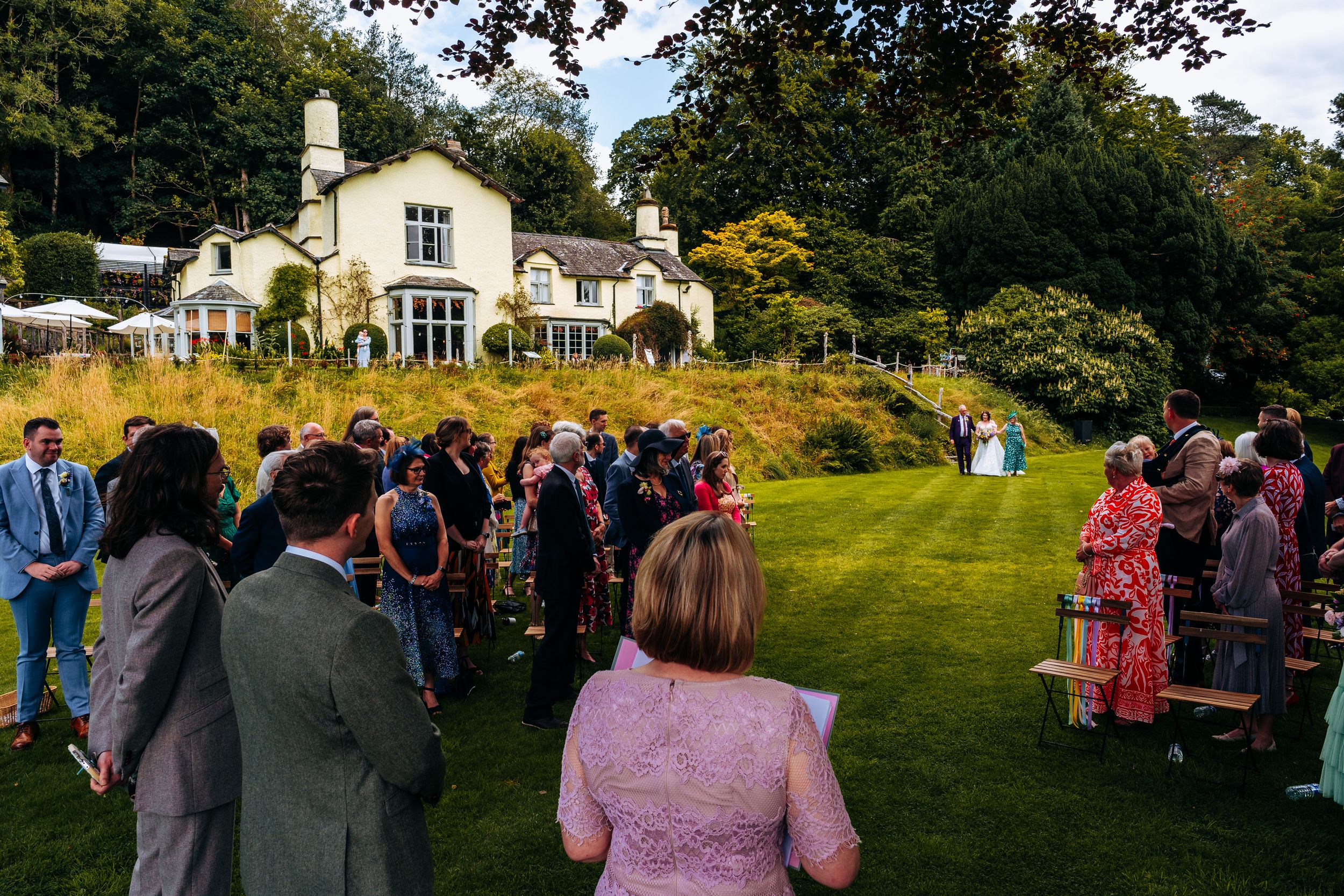 Outdoor garden wedding ceremony at elegant countryside manor house in the Lake distrcit with guests seated on lawn.