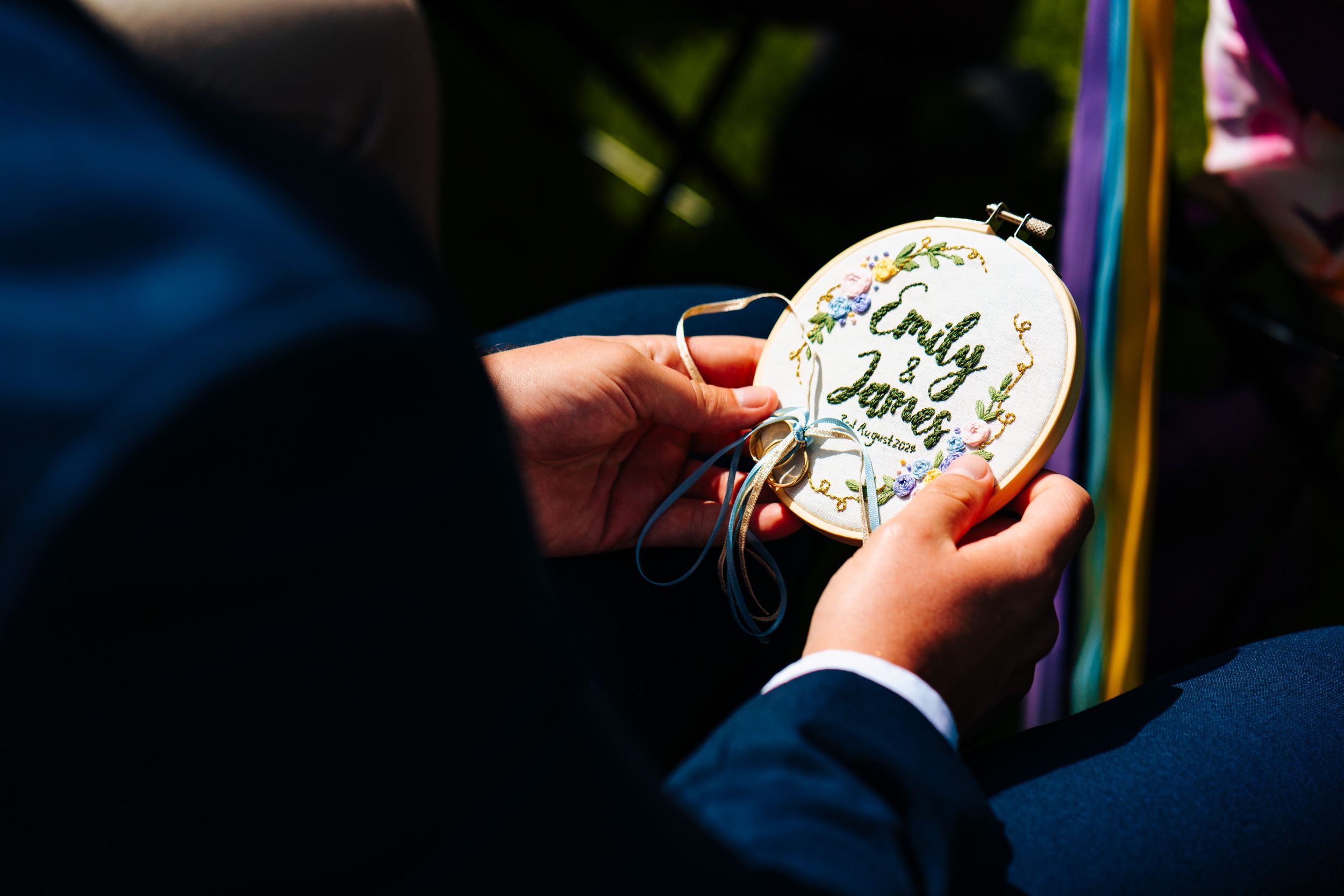 Close-up of embroidered hoop ring bearer pillow with names Emily and James in colorful thread.