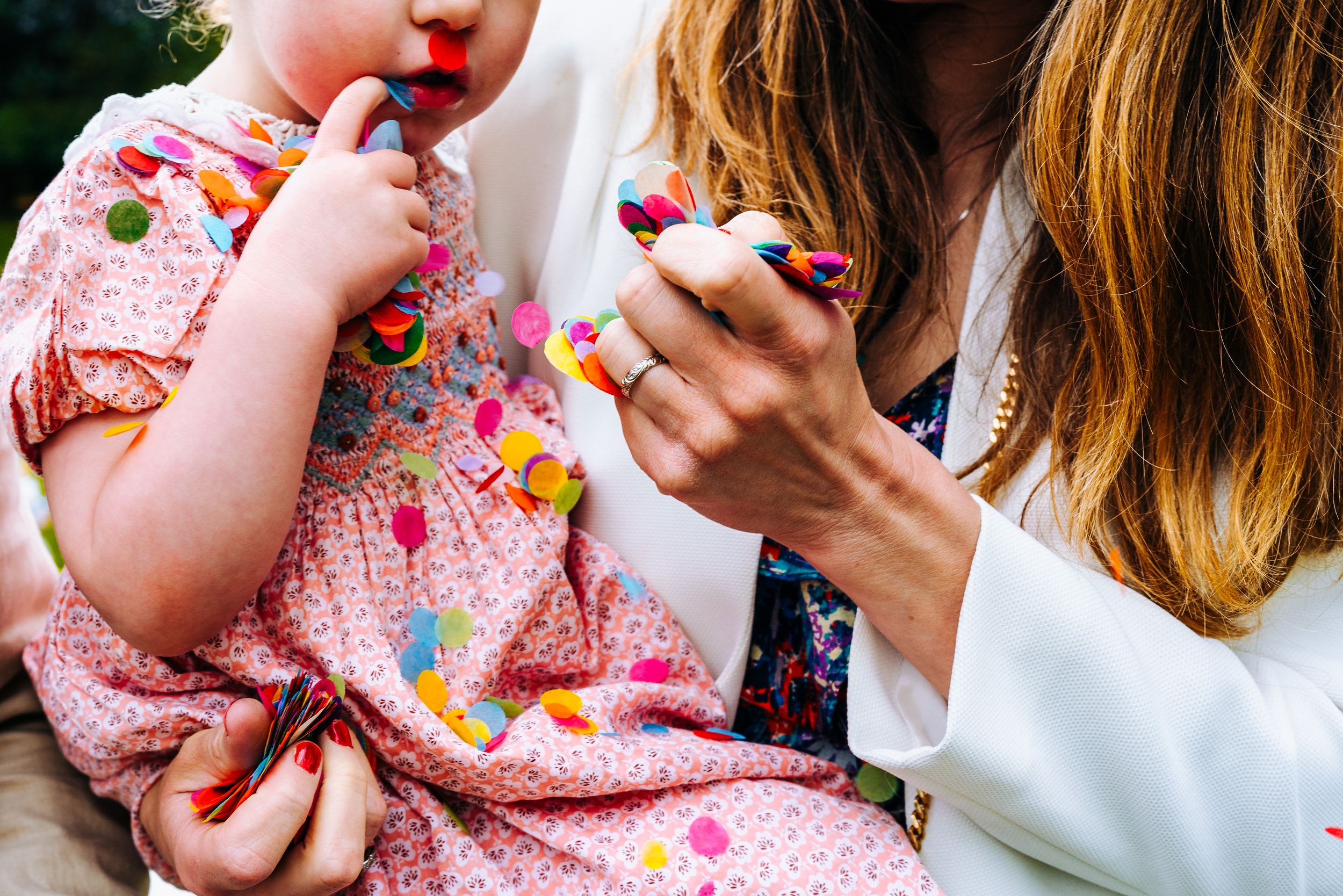 Mother holding toddler in floral dress while both enjoy colorful candy treats together.