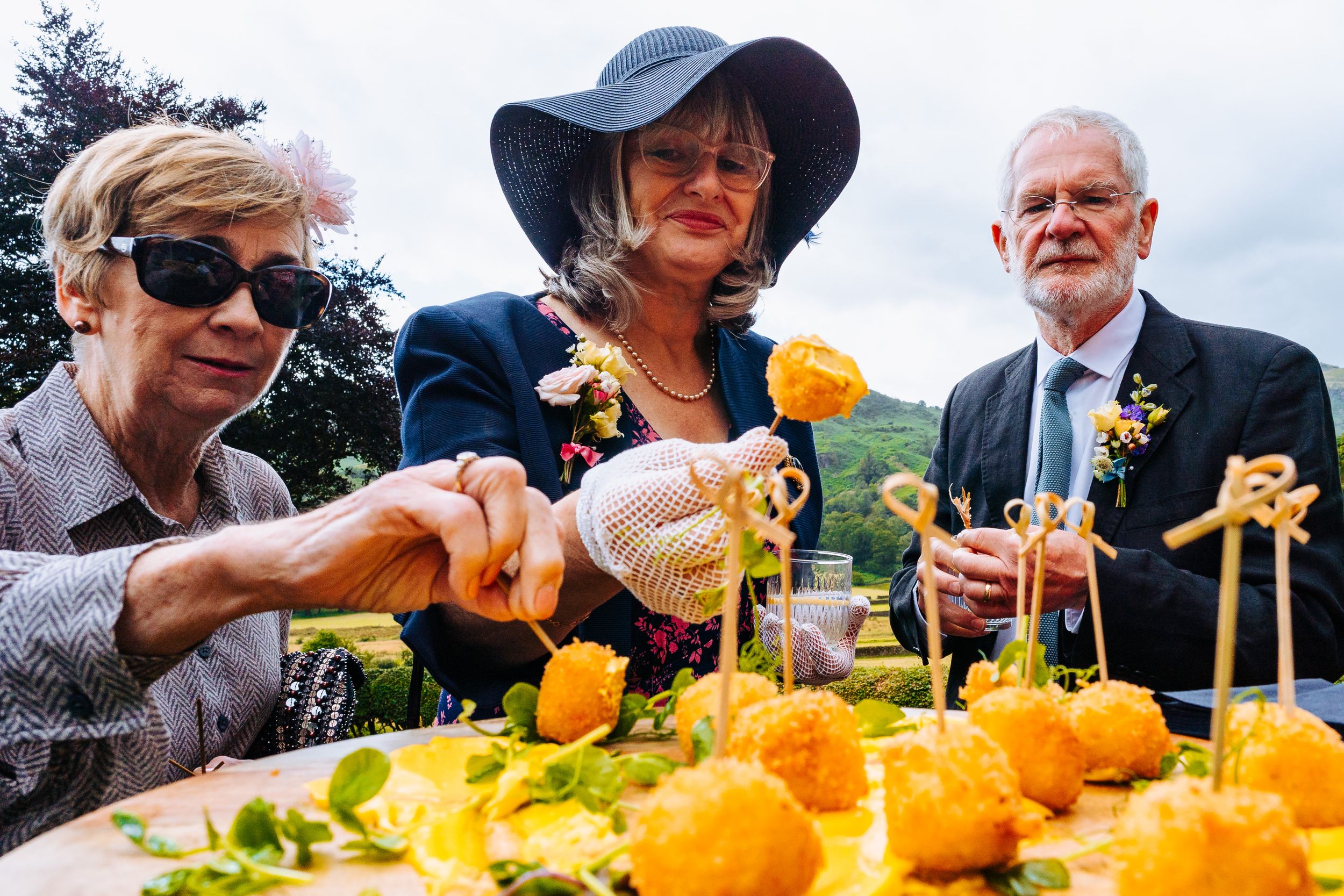 Wedding guests sampling yellow floral appetizers at elegant outdoor cocktail hour display.