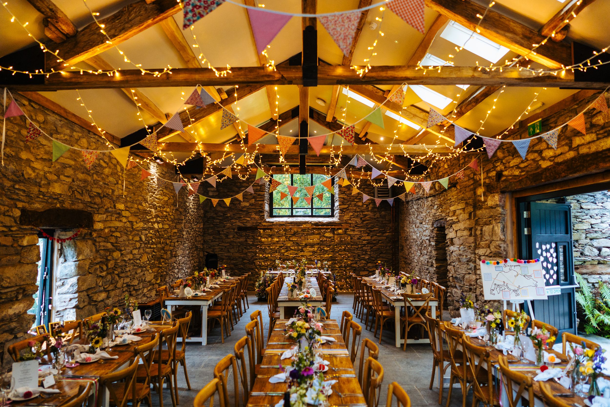 Rustic stone barn wedding reception venue decorated with bunting and fairy lights overhead.