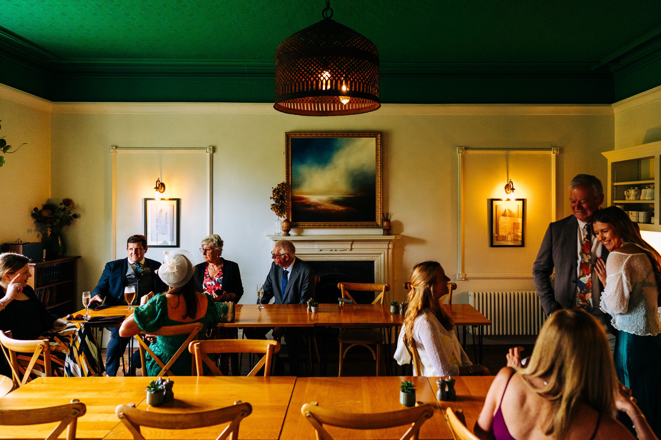 Wedding guests mingling in elegant green-ceilinged reception room with warm wooden furnishings at  the Lancrigg.