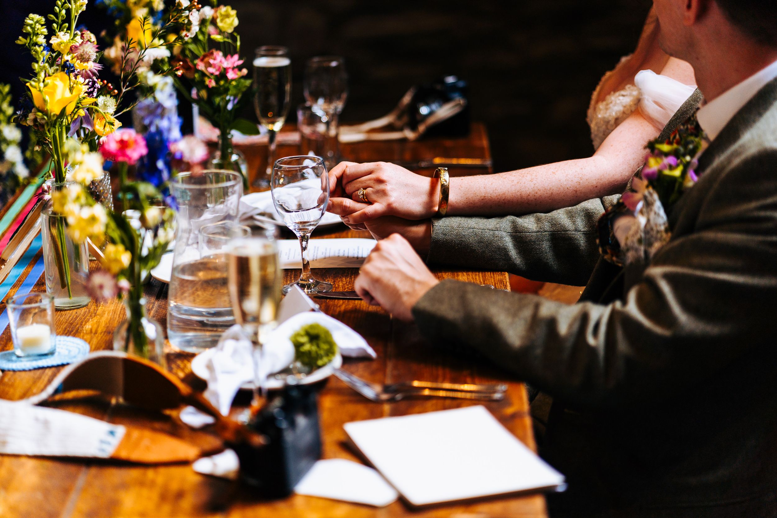 A groom adjusts his cufflinks at a beautifully decorated wedding reception table with colorful flowers.