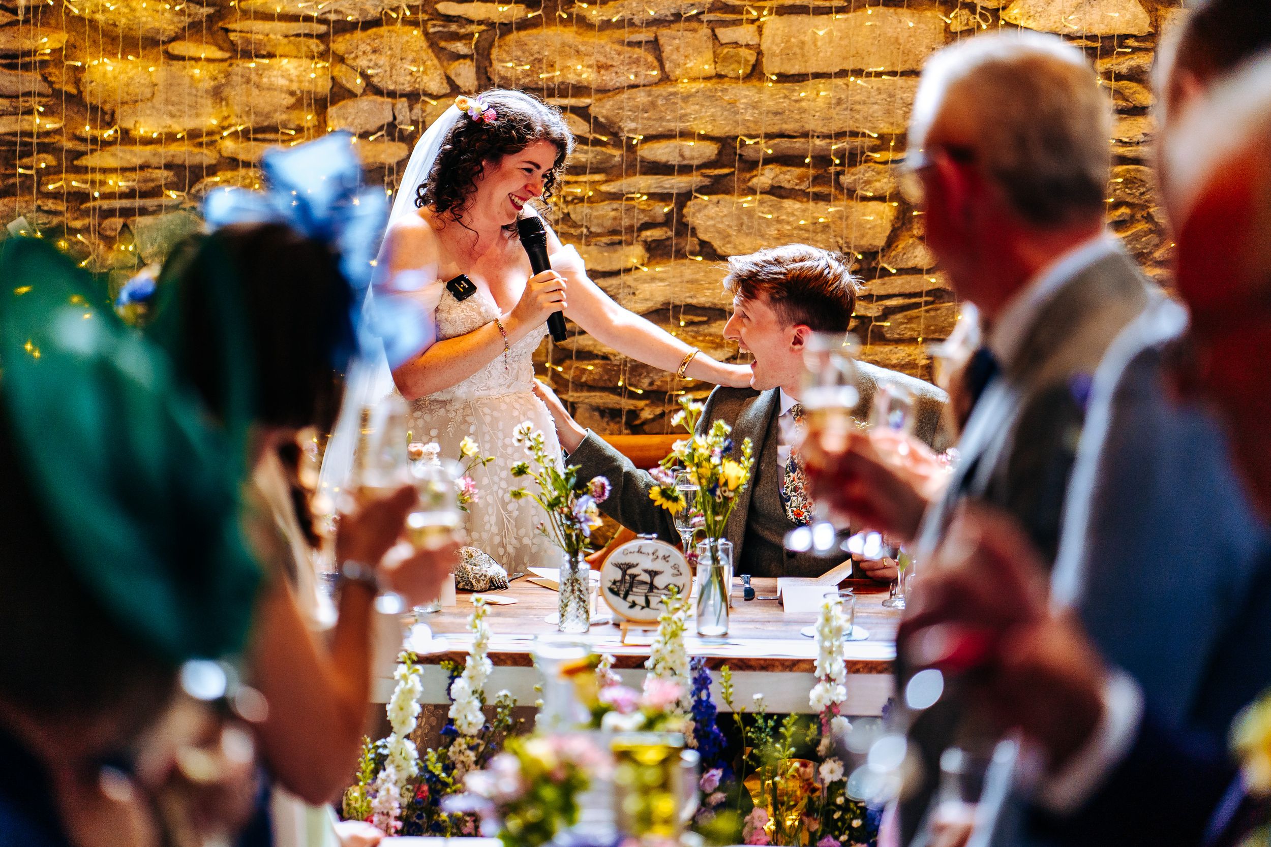 Bride gives a heartfelt speech at the head table while guests raise champagne glasses in celebration.