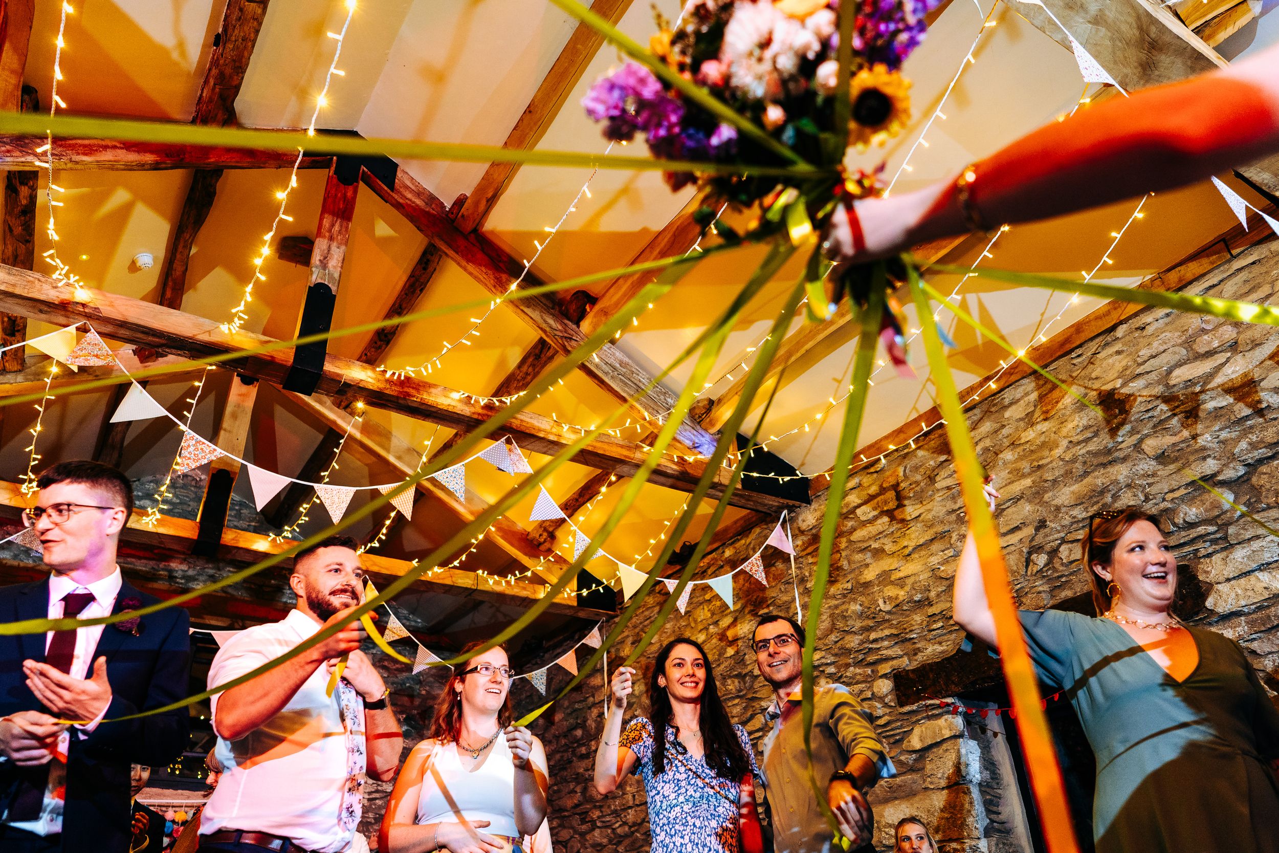 Wedding guests reach up excitedly as the bride tosses her bouquet inside a rustic barn venue.