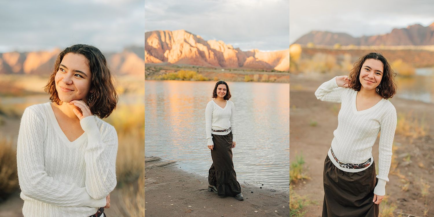 Young woman in white sweater and dark skirt poses near a lake with red rock mountains at golden hour.