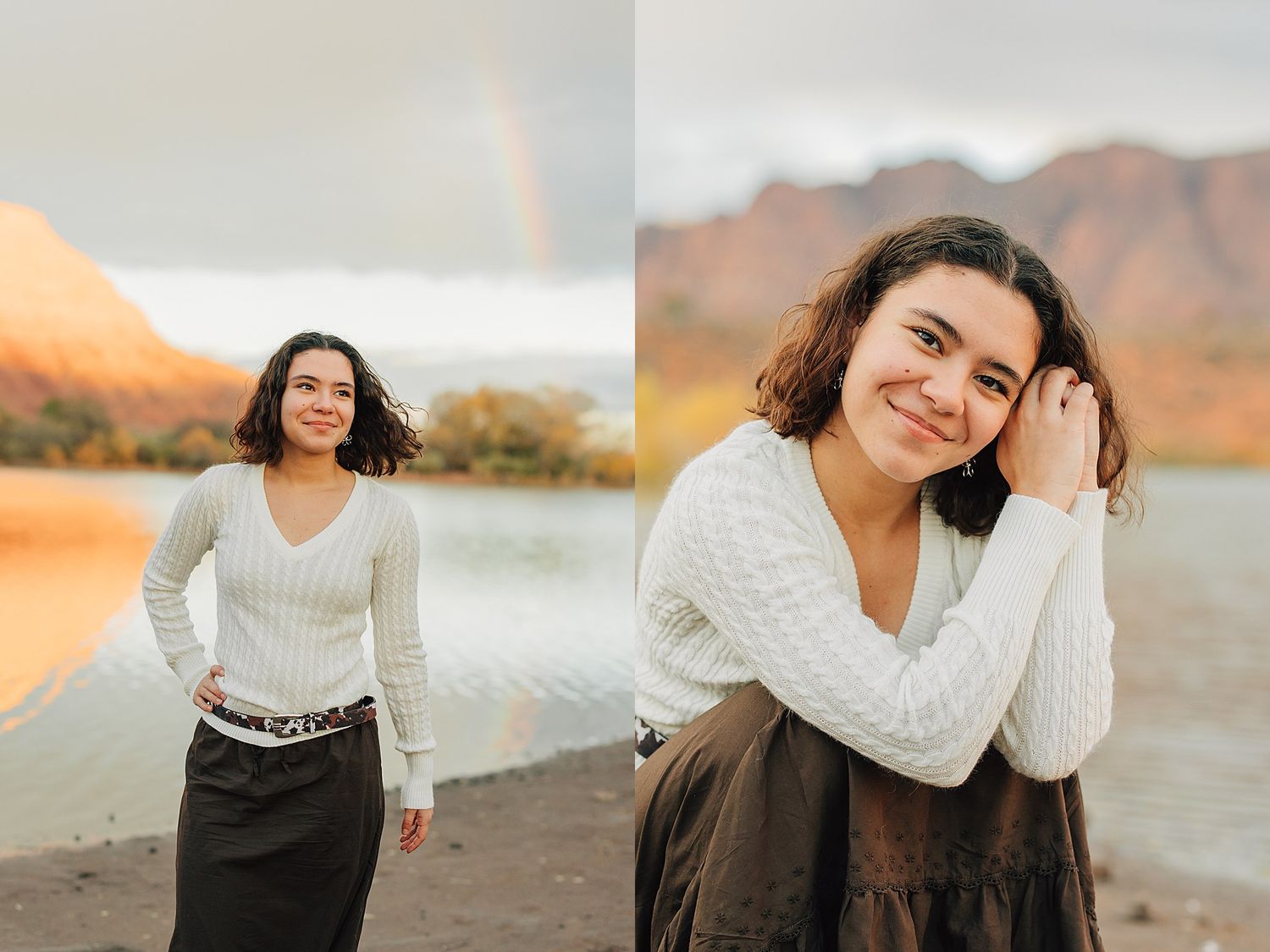 Young woman in white sweater poses near a lake with a rainbow and mountain backdrop in a senior portrait session.
