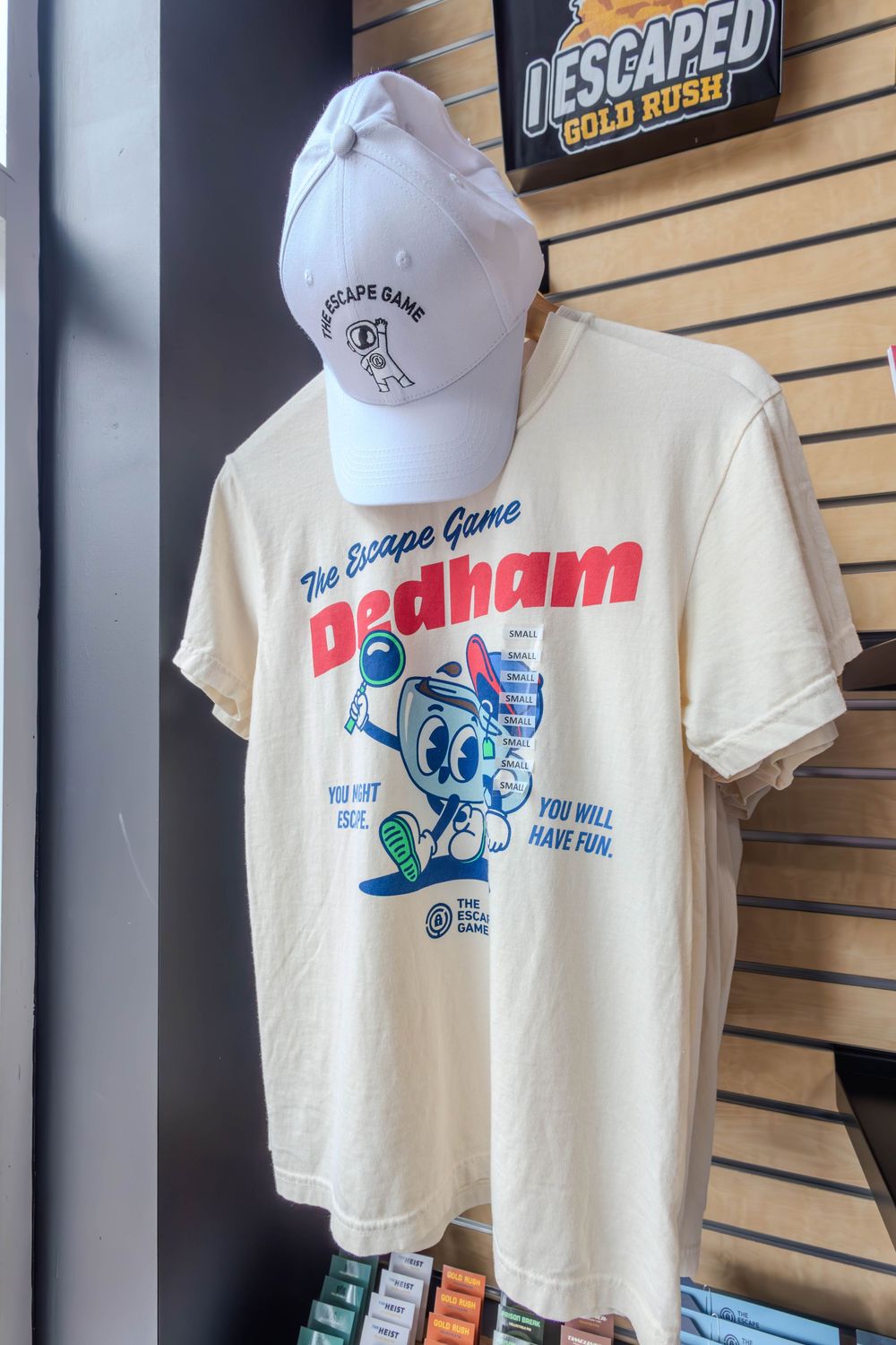 White Escape Game Dedham t-shirt and matching cap displayed on a mannequin in a merchandise store.