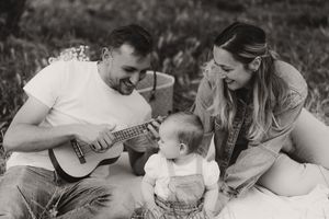 Family enjoying outdoor music time together on white blanket in black and white.