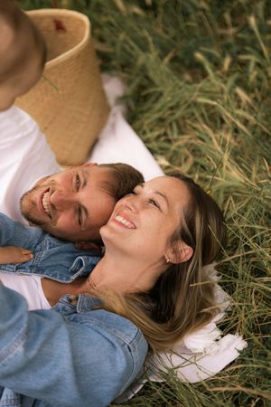 Couple lying on white blanket in grass sharing genuine laughter together.