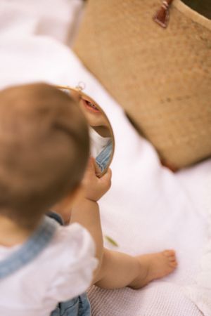 Small child in denim exploring items on white blanket during outdoor photoshoot.