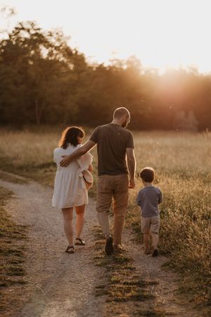 Family walking together on dirt path during golden sunset in nature.