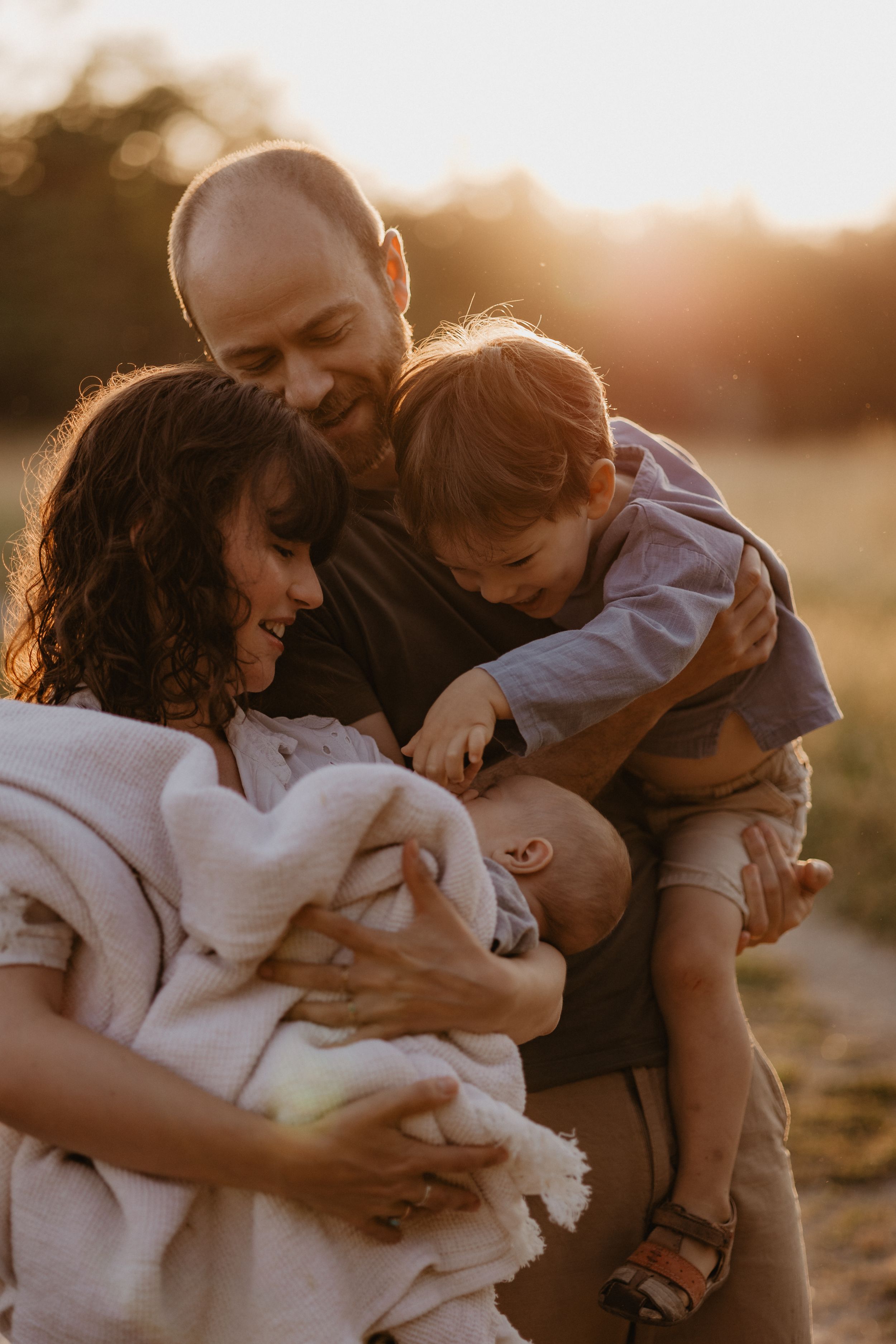 Loving family embracing during golden hour in outdoor field setting.