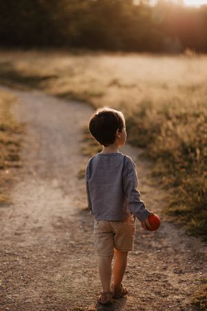 Small child walking alone on dirt path during sunset.
