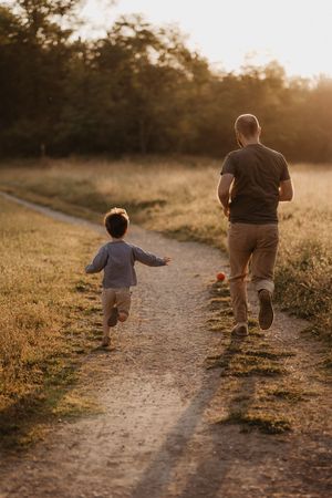 Parent and child running together on dirt path at sunset.