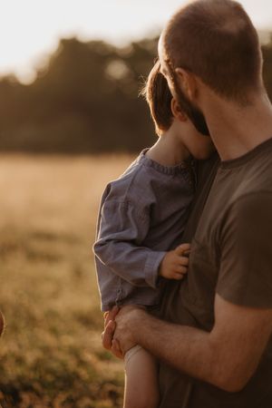 Parent holding child close during sunset in a peaceful meadow.