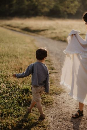 Parent and child walking together on dirt path through golden field.