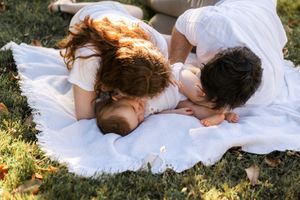 Couple lying together on white blanket in sunny garden setting.